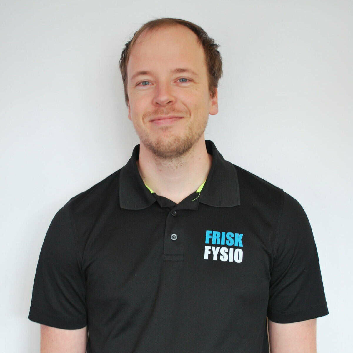 Alt: Portretfoto van Erwin, fysiotherapeut bij Frisk Fysio, lachend en professioneel gekleed, gespecialiseerd in fysio- en revalidatietherapie.