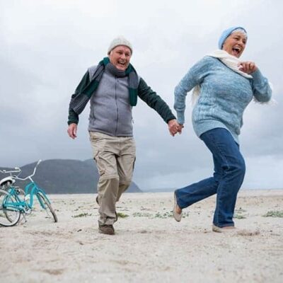 Ouder stel rent hand in hand op het strand.