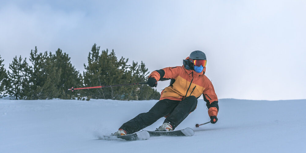 Man in een oranje jas is van een piste aan het skiën tijdens wintersport en draagt warme kleding