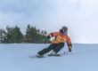 Man in een oranje jas is van een piste aan het skiën tijdens wintersport en draagt warme kleding