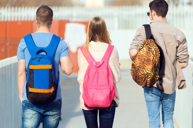 drie studenten lopen terug naar school met hun rugtas op en voorkomen Nek- en schouderklachten.