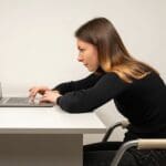 Vrouw gekleed in het zwart werkt met een gebogen rug achter haar laptop en loopt zo kans op hoge rugpijn.