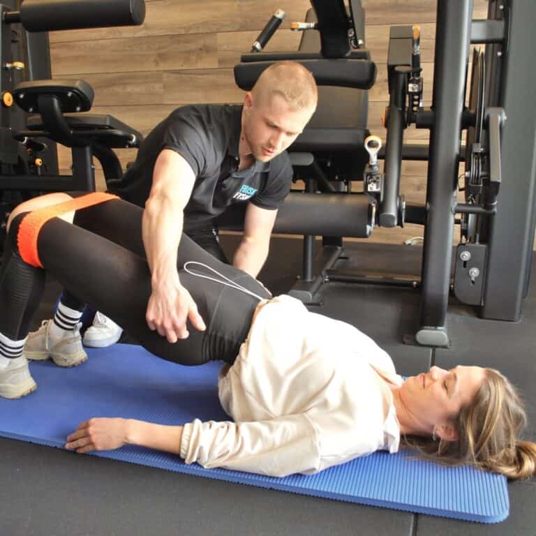 Fysiotherapie behandeling met trainer en patiënt in een sportschool voor revalidatie en fysieke fitness | Professionele fysiotherapeut voert oefening uit op een matje met hulpmiddelen voor herstel | Optimaliseer je herstel en beweegkracht bij Frisk Fysio.