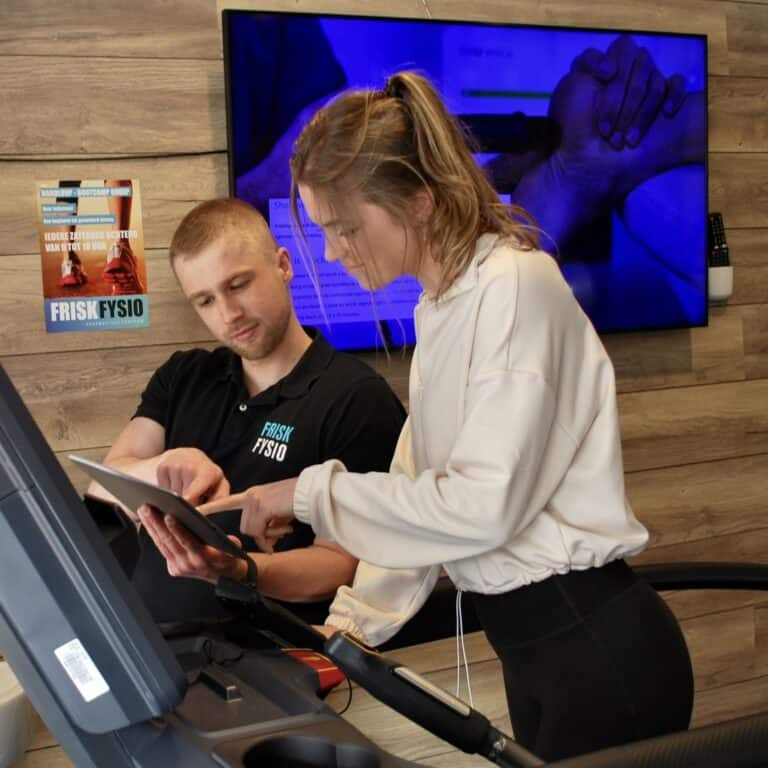 Cycling trainer in a physiotherapy practice at FRISK FYSIO, with an instructor and client discussing the workout, aimed at recovery and fitness improvement.