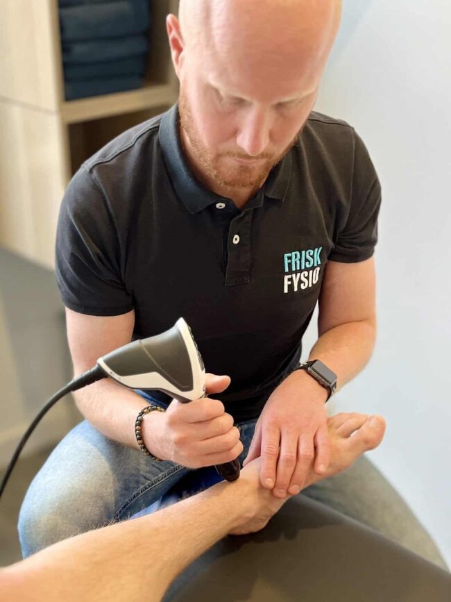 Middelbare leeftijd man krijgt fysiotherapie op zijn hand in een kliniek, begeleid door professionele fysiotherapeut, behandeling voor hand- en polsblessures, herstel en revalidatie, orthopedische fysiotherapie, praktijk Frisk Fysio, gezondheidszorg, sportblessures.