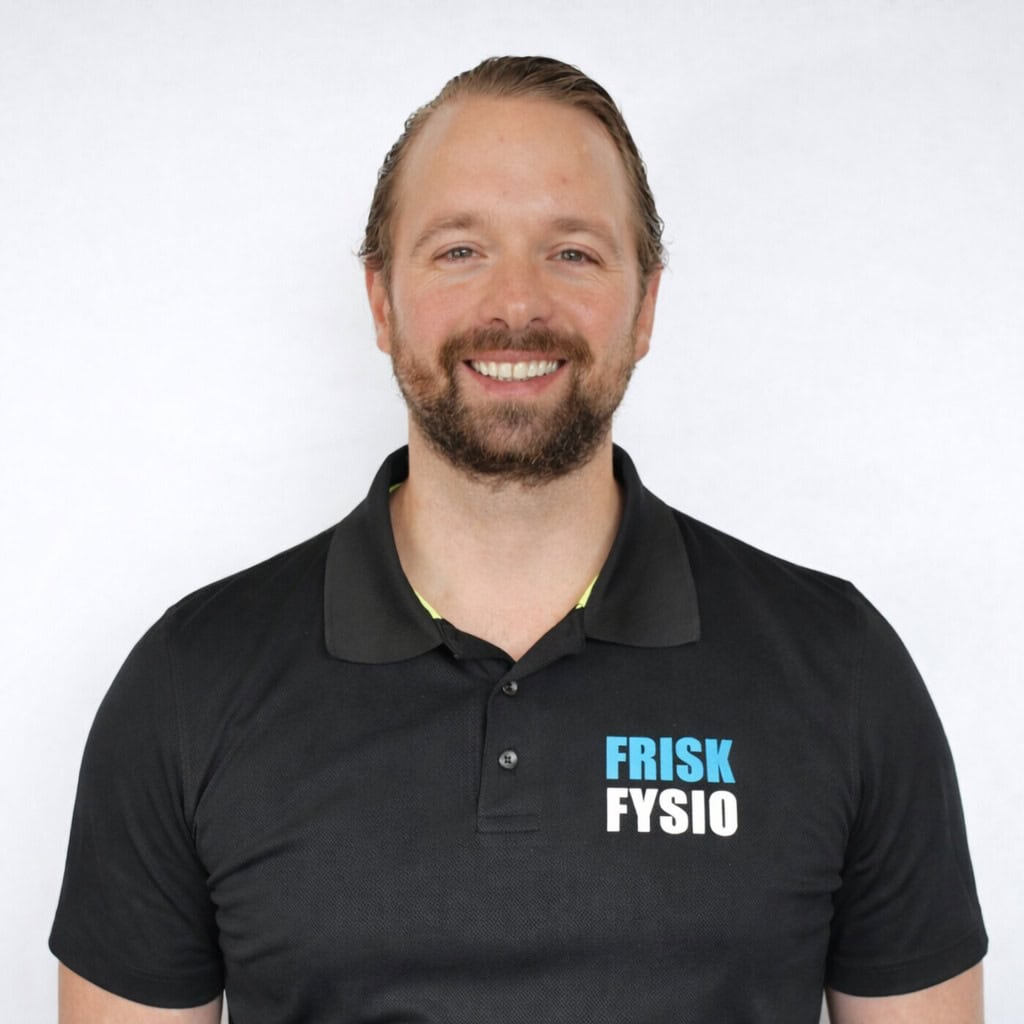 Portret van Randy, fysiotherapeut bij Frisk Fysio, lachend en professioneel, in zwart uniform met logo.