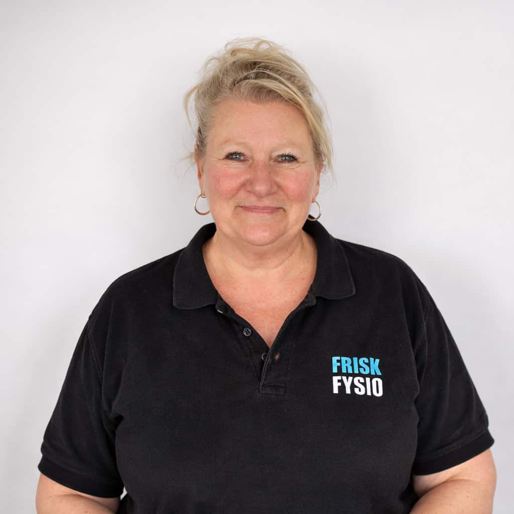 Fysiotherapeut Pascal bij Frisk Fysio Vrouwelijke fysiotherapeut Pascal van Frisk Fysio, lachend en professioneel gekleed in een zwart polo met het Frisk Fysio logo, poseert in een kliniekomgeving.