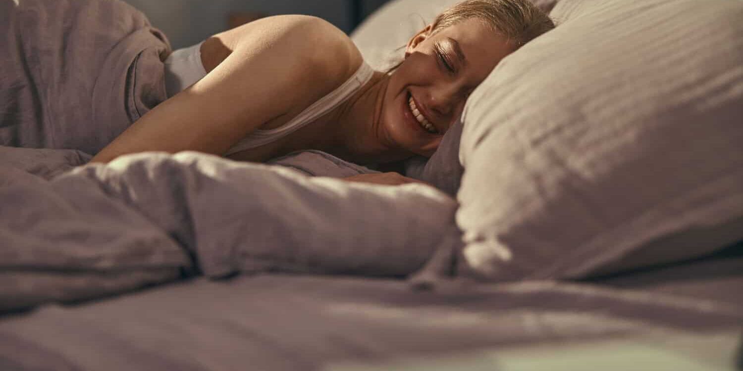 Woman smiles in bed due to sleep and muscle recovery
