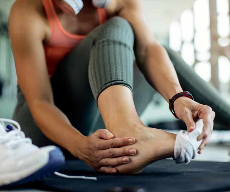 Vrouw in groene sportbroek trekt haar sok uit, zodat ze kan voelen aan haar enkelverzwikking.