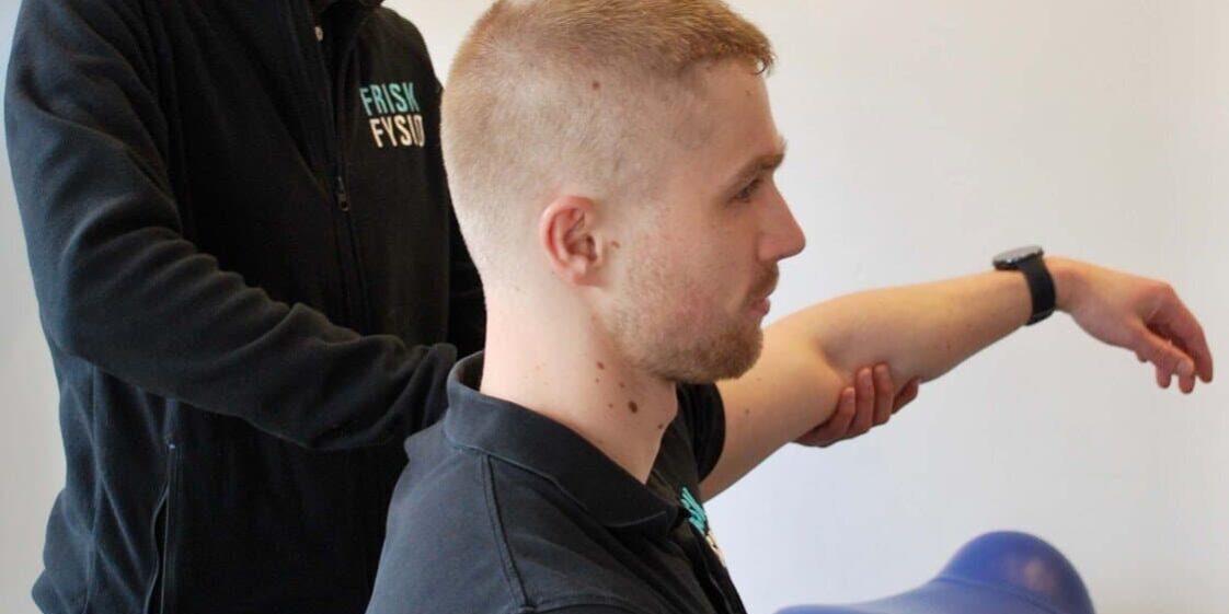 Vrouwelijke fysiotherapeut helpt een man in zwart shirt met oefeningen tegen een peesontsteking in de schouder.