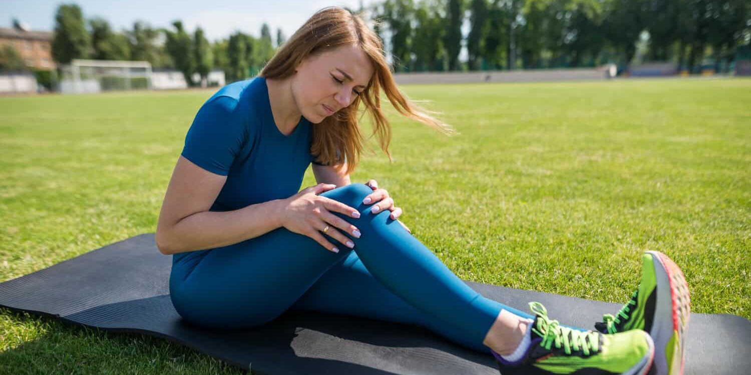 Woman in blue sports leggings, holds her knee. She is suffering from a torn meniscus.