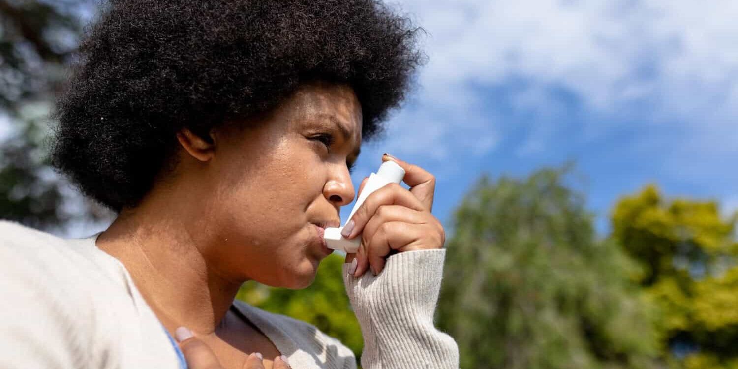 Woman in beige vest, is taking a puff for her asthma symptoms while moving.