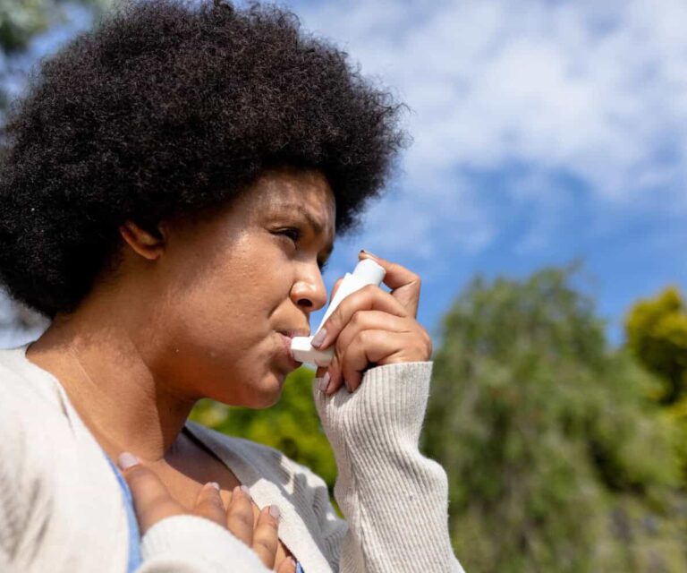 Vrouw in beige vest, is een pufje aan het nemen voor haar astma klachten tijdens het bewegen.
