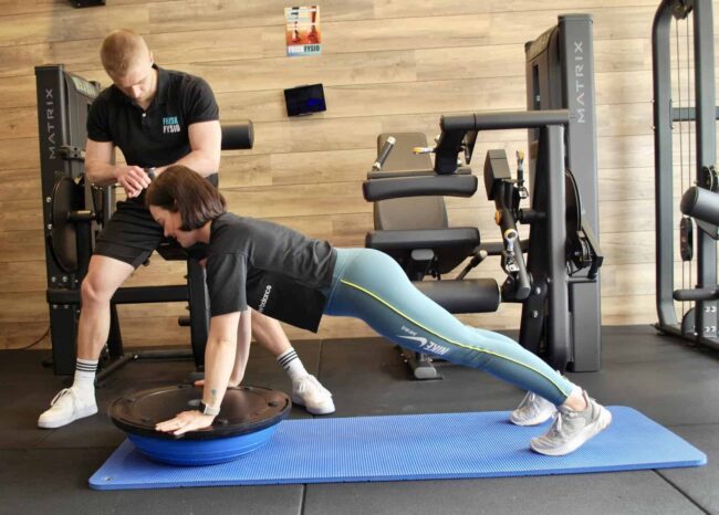 Fysiotherapie oefening met trainer en cliënt Fysiotherapie helpt vrouw met bewegen om blessures in de sportschool te voorkomen.