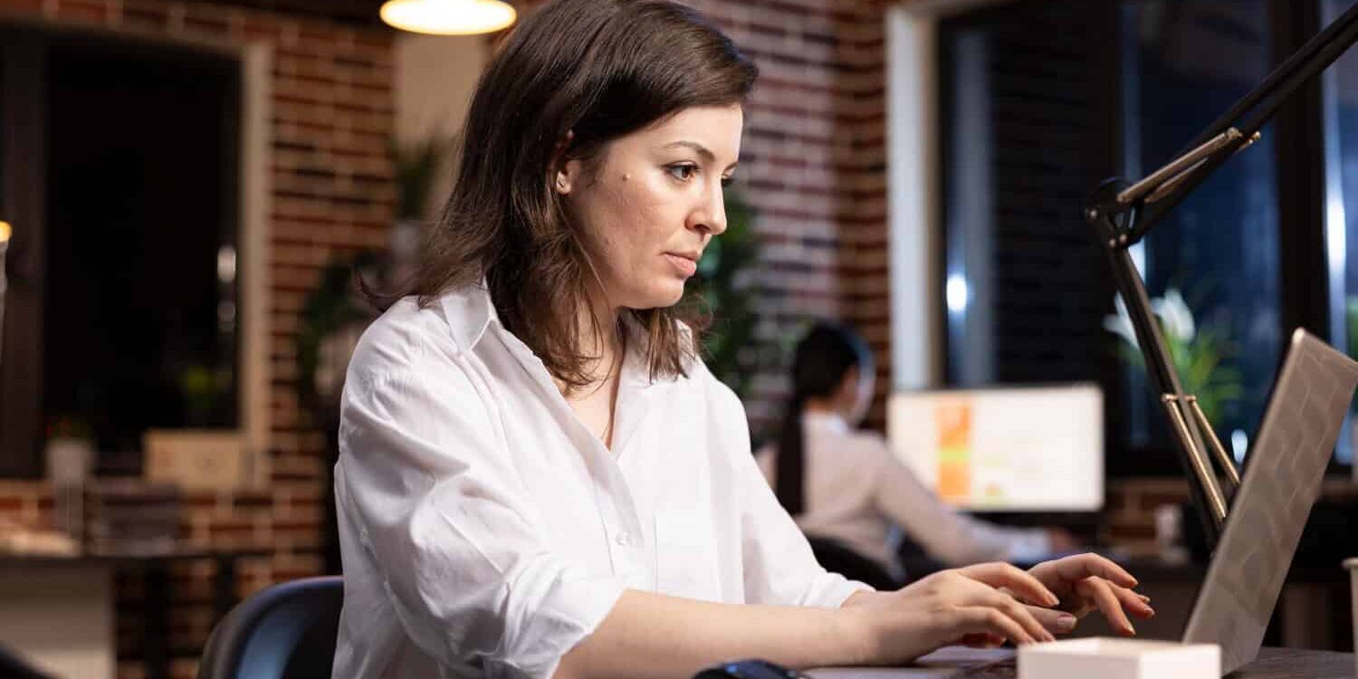 Werkstress en burn-out herstel Vrouw zit achter haar laptop met een gestresst gezicht door klachten bij een burn-out.