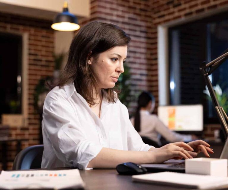 Vrouw zit achter haar laptop met een gestresst gezicht door klachten bij een burn-out.