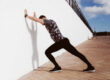 Man stands against the wall doing his daily stretching exercises.