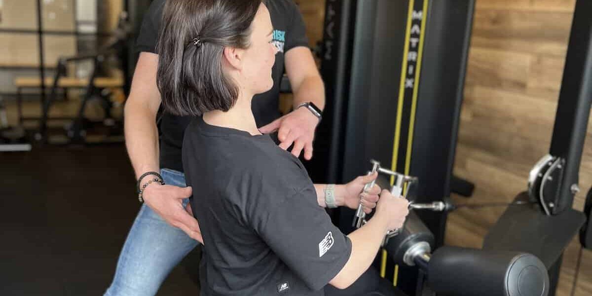 Persoonlijke training bij FriskFysio Fysiotherapeut helpt een vrouw in de sportschool om beginnende blessure te voorkomen.