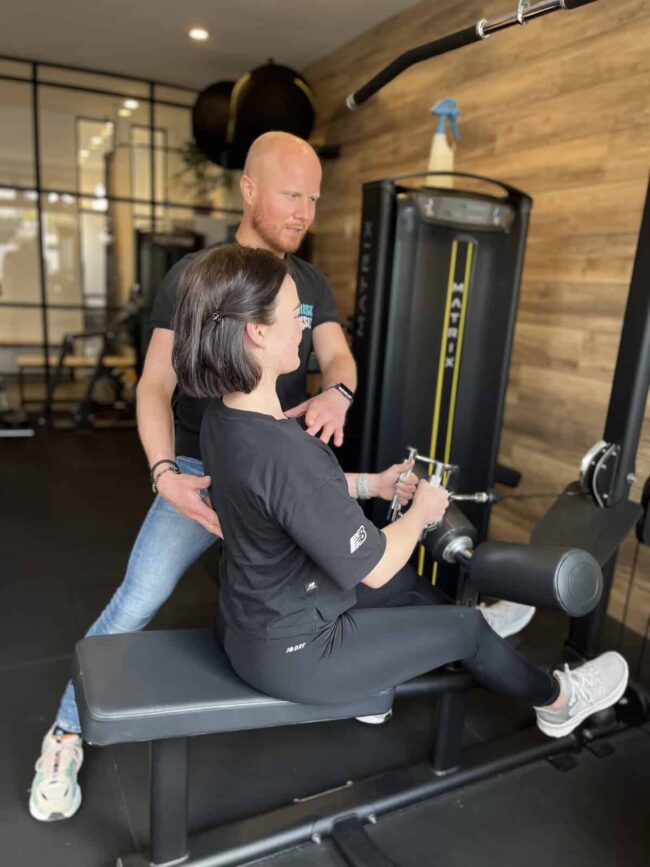 Persoonlijke training bij FriskFysio Fysiotherapeut helpt een vrouw in de sportschool om beginnende blessure te voorkomen.