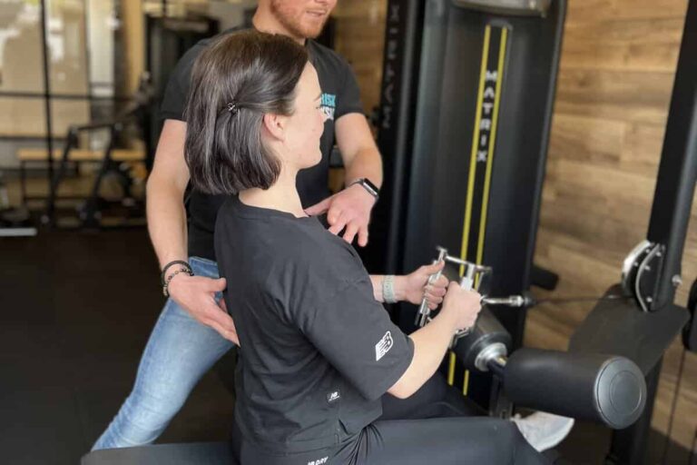 Fysiotherapeut helpt een vrouw in de sportschool om beginnende blessure te voorkomen.