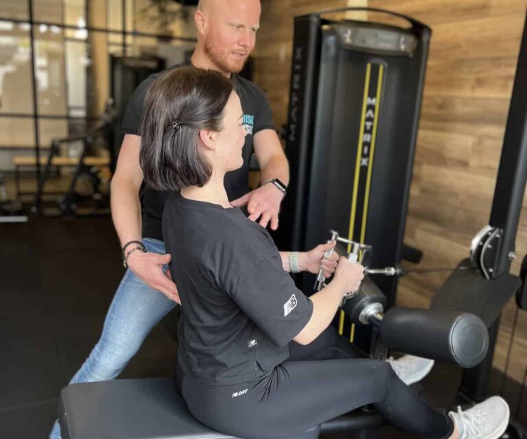 Persoonlijke training bij FriskFysio Fysiotherapeut helpt een vrouw in de sportschool om beginnende blessure te voorkomen.