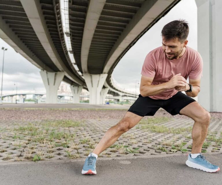 Man probeert Kramp in de kuiten te voorkomen en doet een oefening buiten onder de viaduct in een roze shirt met sportschoenen
