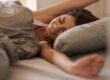 Vrouw rekt uit in bed en moet oppassen voor een stijve nek bij het opstaan.