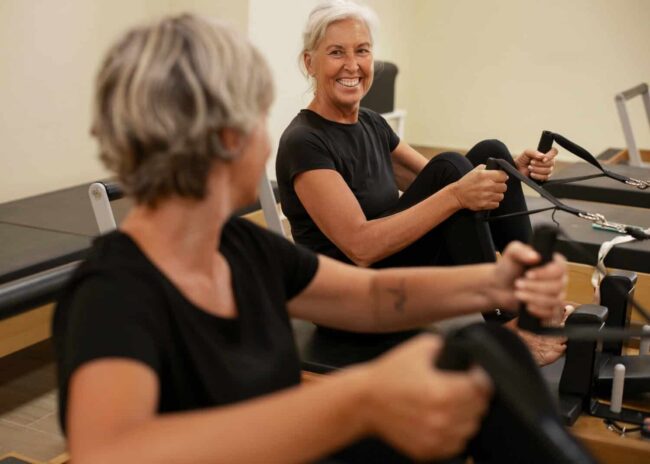 spierkracht behouden na je 60e Twee oudere vrouwen doen sporten voor om te laten zien hoe je spierkracht behouden na je 60e