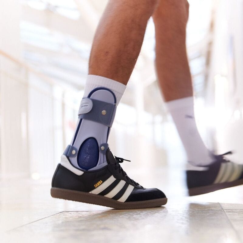 CaligaLoc enkelorthese 3 Friktionele enkelorthese met scharnier en bandjes, gedragen met een sportieve schoen op een glanzende vloer.