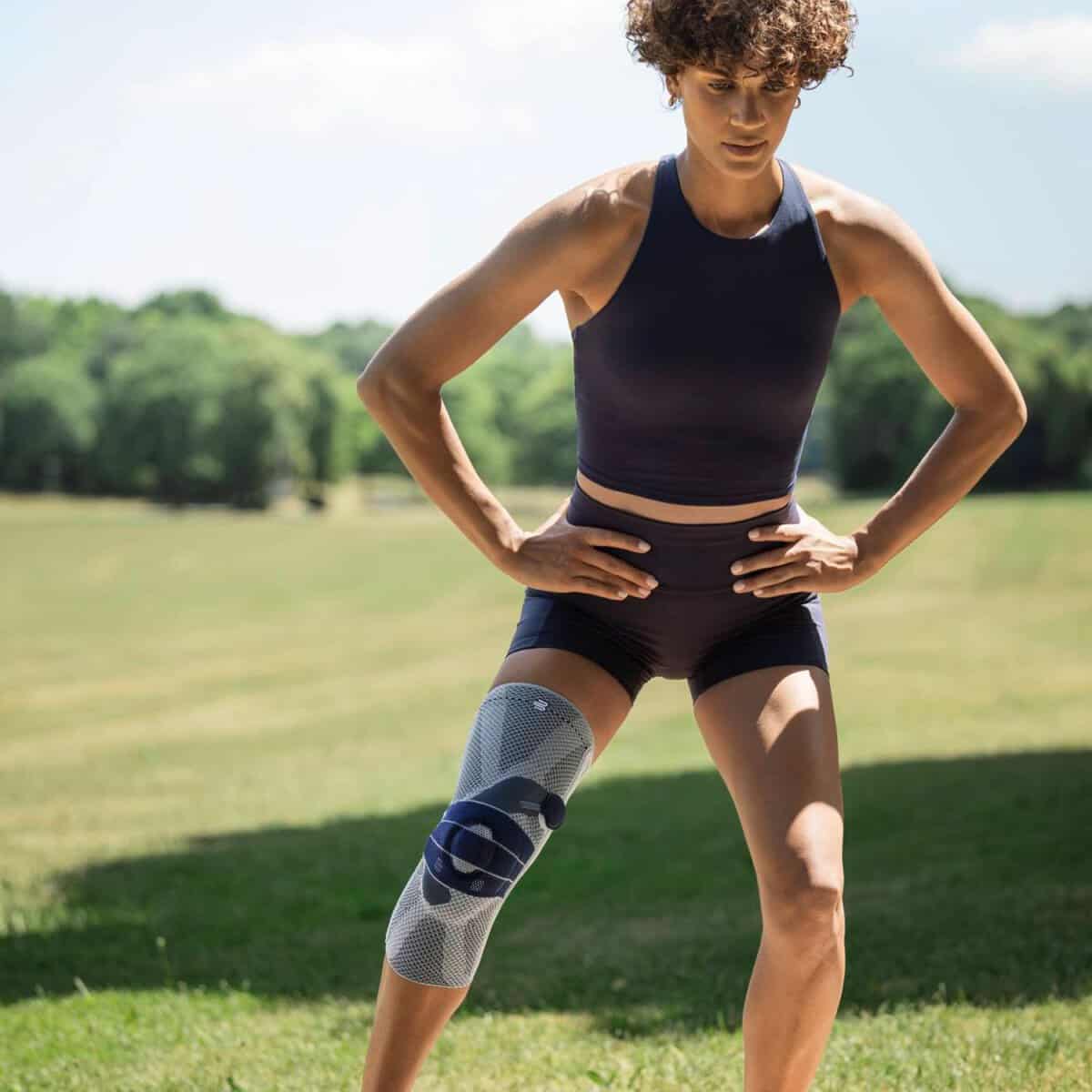 GenuTrain P3 kniebrace 3 Atleet met kniebrace op de rechterknie tijdens outdoor training in een groene, zonovergoten omgeving.