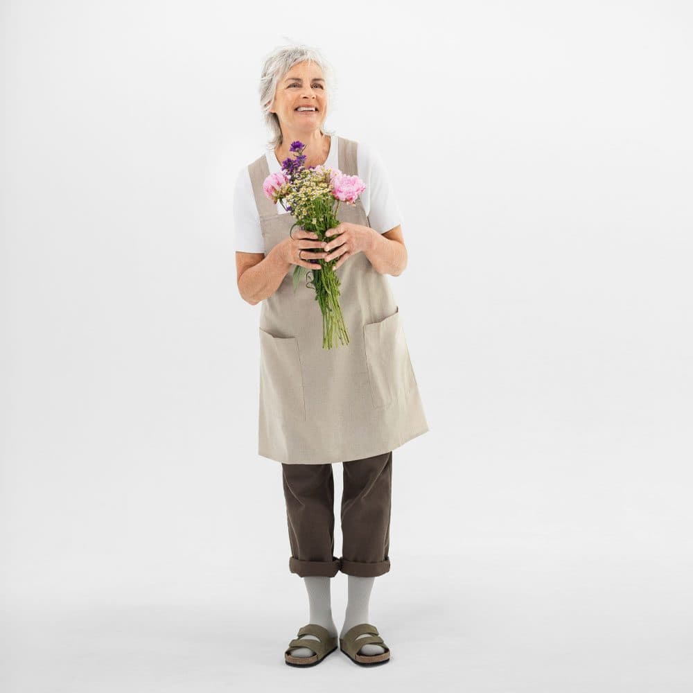 VenoTrain® hero 9 A cheerful elderly woman is holding a bunch of flowers, wearing a beige apron and light-coloured clothes, and smiling at the camera.