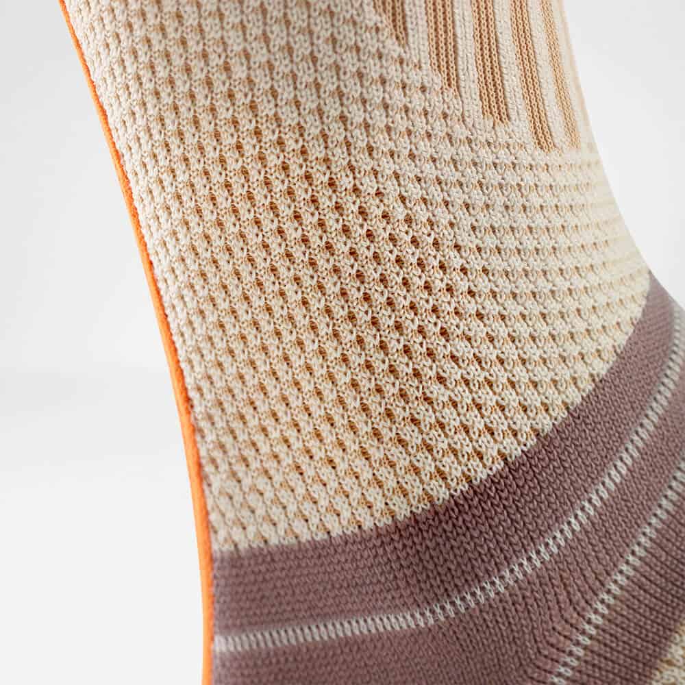 Outdoor Ankle Support 7 Dichte, gebreide knie- of enkelbrace of sportskousen in beige met oranje rand en roze-taupe band, close-up textuur en meshpatroon.