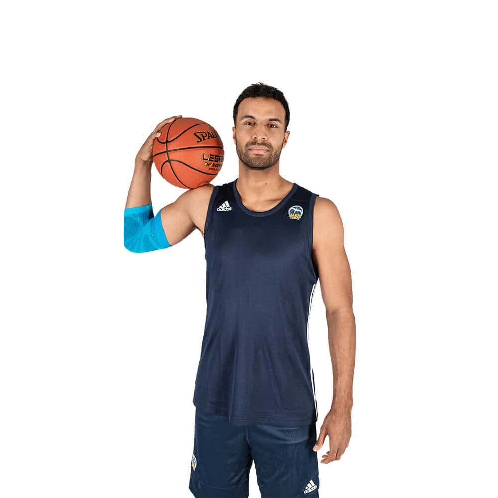 Sports Compression Elbow Support 6 Speler in donkerblauw basketbaltenue met bal op linker schouder, sportief posed voor fysiotherapie en sportgezondheid context.