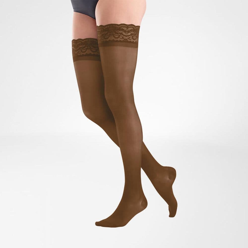 VenoTrain® act SHEER ELEGANCE AG 1 Damesbenen in bruine, doorzichtige aansluitende panty's met kanten bovenkant, model staand tegen lichte achtergrond.