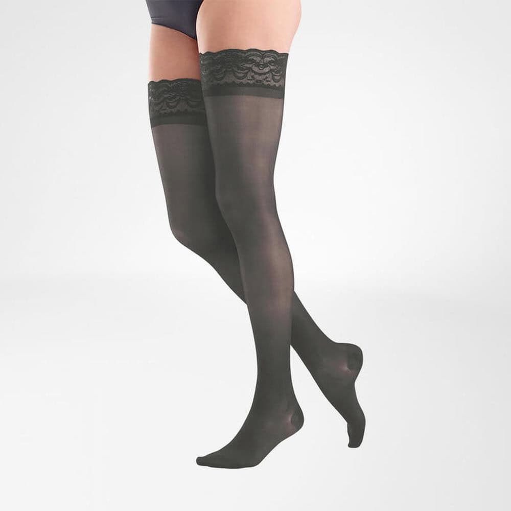 VenoTrain® act SHEER ELEGANCE AG 2 Damesbenen draagend zwarte kousen met kanten boord, knieën gebogen, witte achtergrond.
