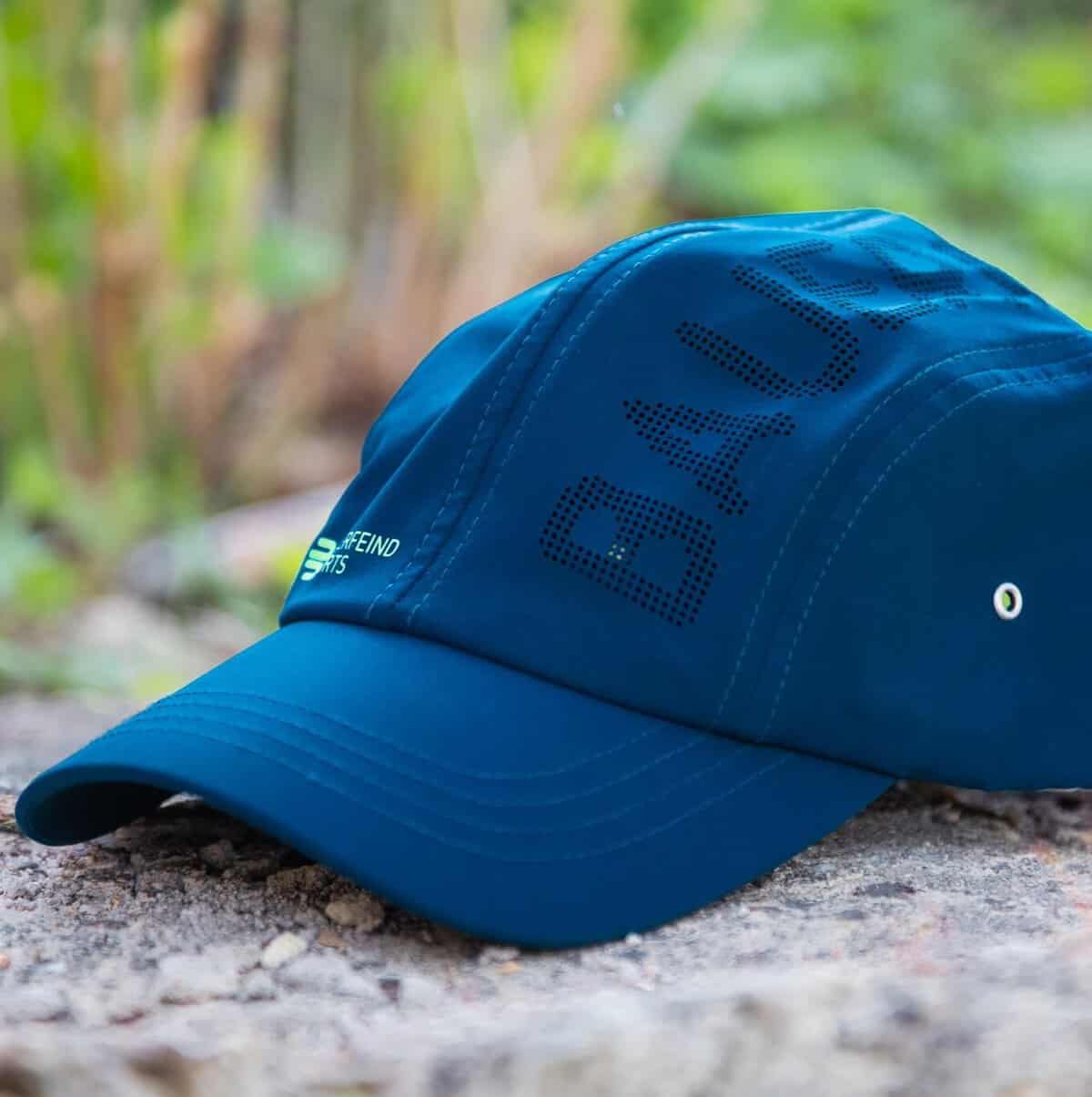 Sports Cap 3 Blauwe cap met geborduurd merk Buck op zandige ondergrond, Buiten in groene tuin, dagelijks gebruiksaccessoire voor sport en ontspanning.