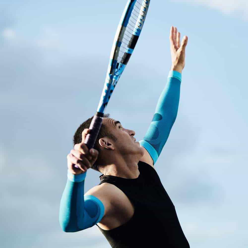 Sports Compression Sleeves Arm 5 Tennisser slaat krachtige slag met blauwe armverbindingen en grip tijdens training op het veld, heldere hemel op de achtergrond.