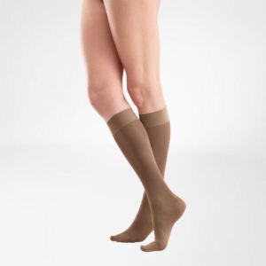 Medische kousen tot net onder de knie gedragen door benen, model staan op een lichte achtergrond.