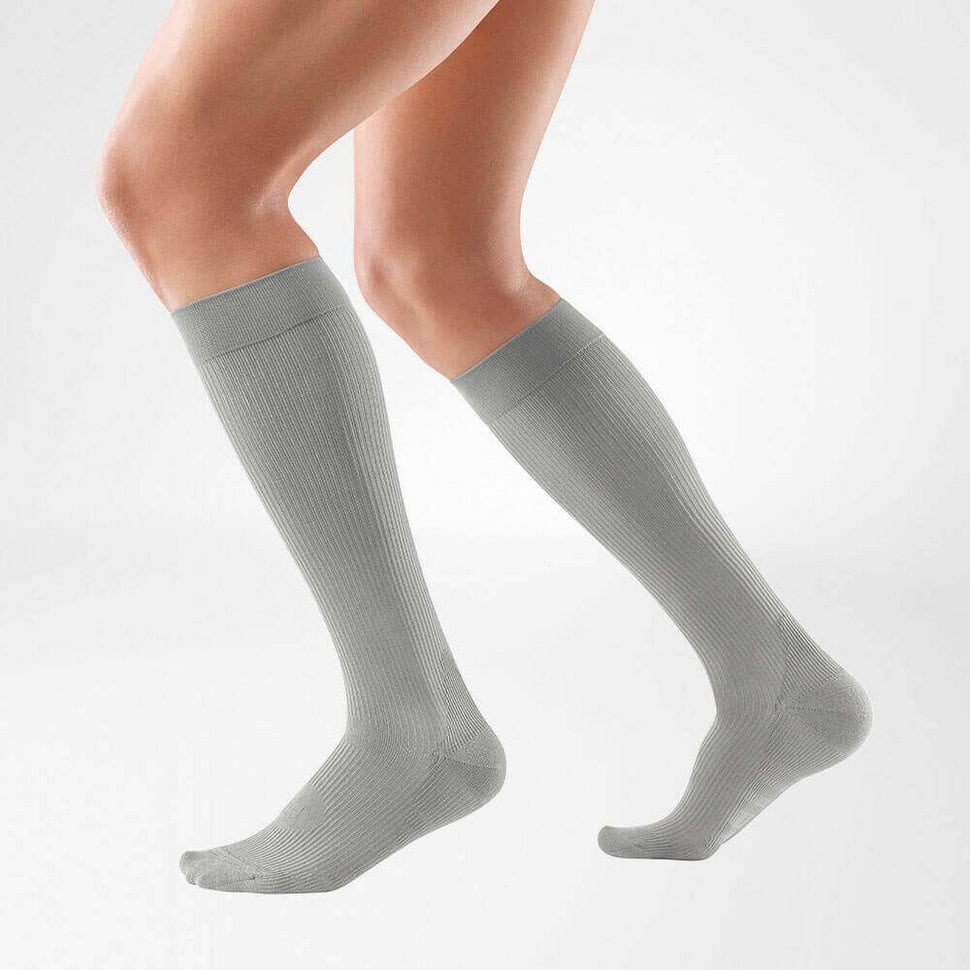 VenoTrain® hero 8 Someone is wearing grey, ribbed, knee-high compression socks, with the left and right socks visible against a white background.