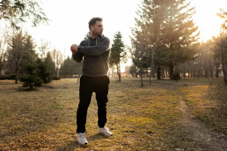 Man stretching outdoors in autumn Man staat zich buiten te rekken en moet uitkijken voor spier- en gewrichtspijn door de kou.