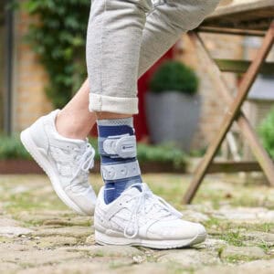 Man met enkelbrace en witte sneakers stap op stenen pad buiten, gericht op enkelondersteuning en herstel.