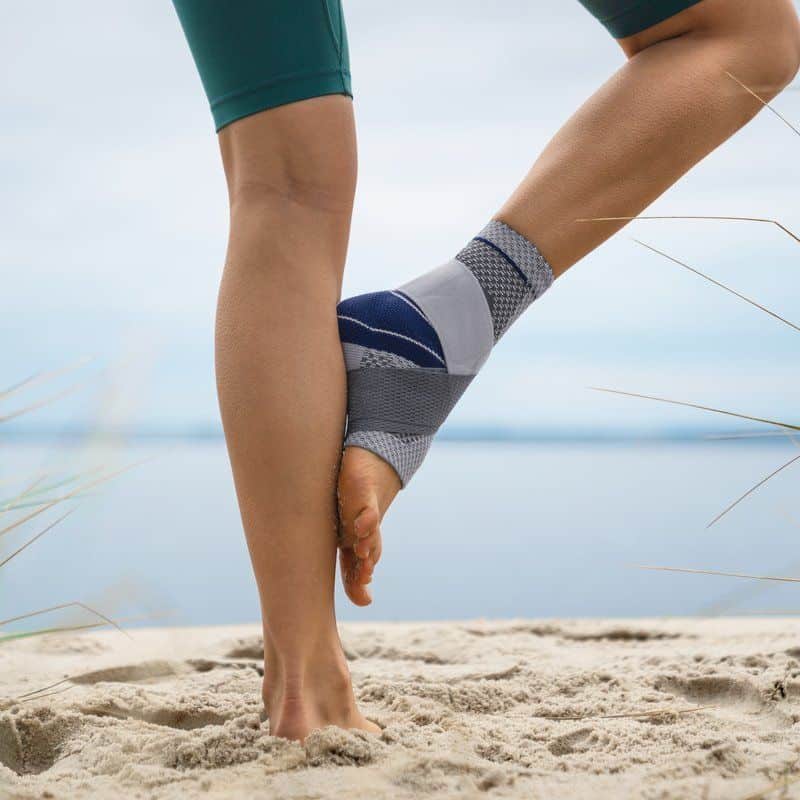 MalleoTrain Plus enkelbrace 6 Frisse enkel en onderarm met sportbrace op het strand, focus op ondersteuning en stabiliteit tijdens beweging.