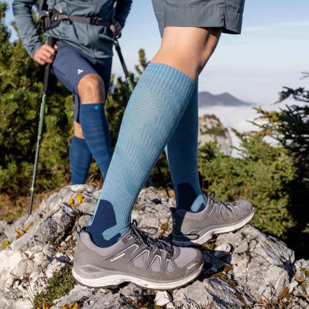 Outdoor Merino Compression Socks 5 Three athletes who look as though they are out walking on a rocky mountain path, carrying rucksacks and walking sticks; low angle shot, focusing on high-quality walking boots and compression socks.