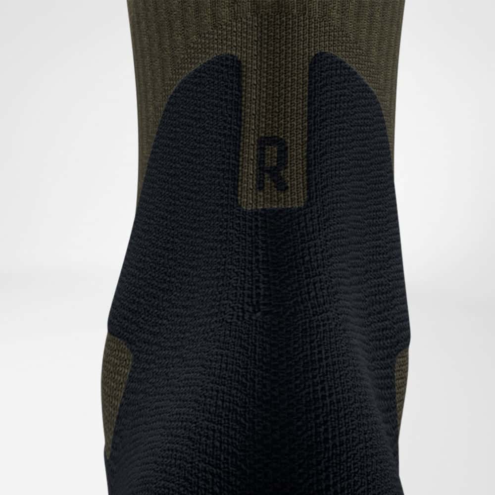 Outdoor Merino Mid Cut Socks 6 Technische sportbroek of compressiesok met zwarte gespikkelde textuur en groene bielastische bovenkant, uitsluitend zichtbaar vanaf de achterkant.