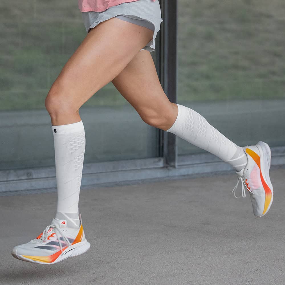 Run Performance Compression Socks 5 Sportieve benen en witte scheenbeschermers tijdens hardlopen buiten, close-up van de onderbenen en schoenen.