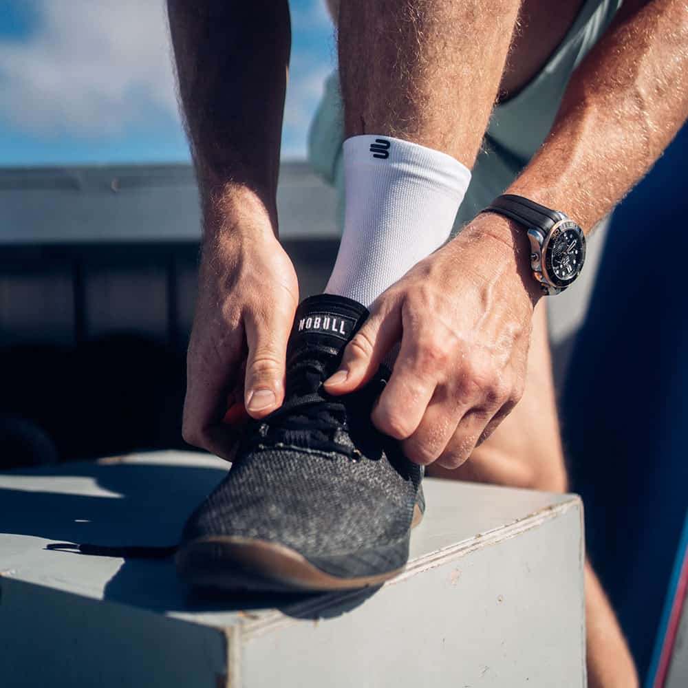 Run Ultralight Mid-Cut Socks 5 A person is tying their trainers during a training session; a sports watch is visible; the focus is on the foot and the laces.