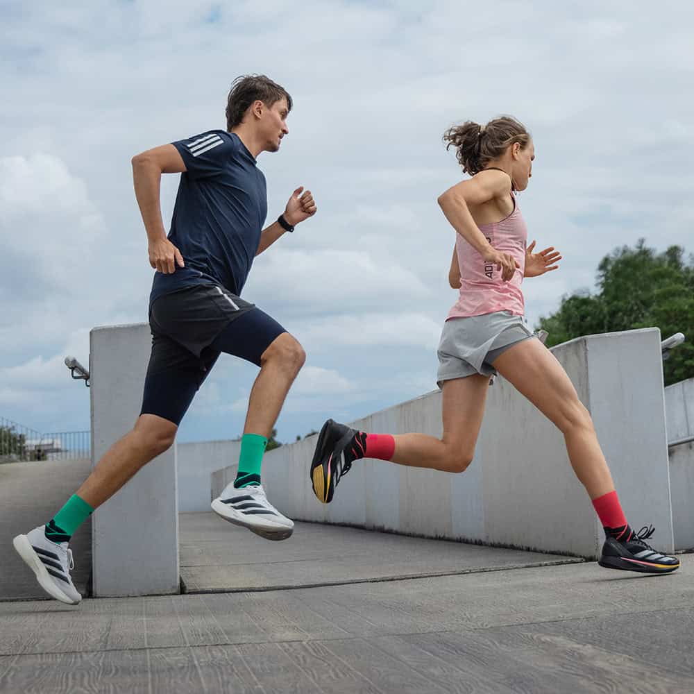 Run Performance Mid Cut Socks 6 Frisse halterende man en vrouw rennen op een buitenweg tijdens een trainingssessie bij FRISKFYSIO, met sportkleding en kleurrijke sokken voor optimale zichtbaarheid.