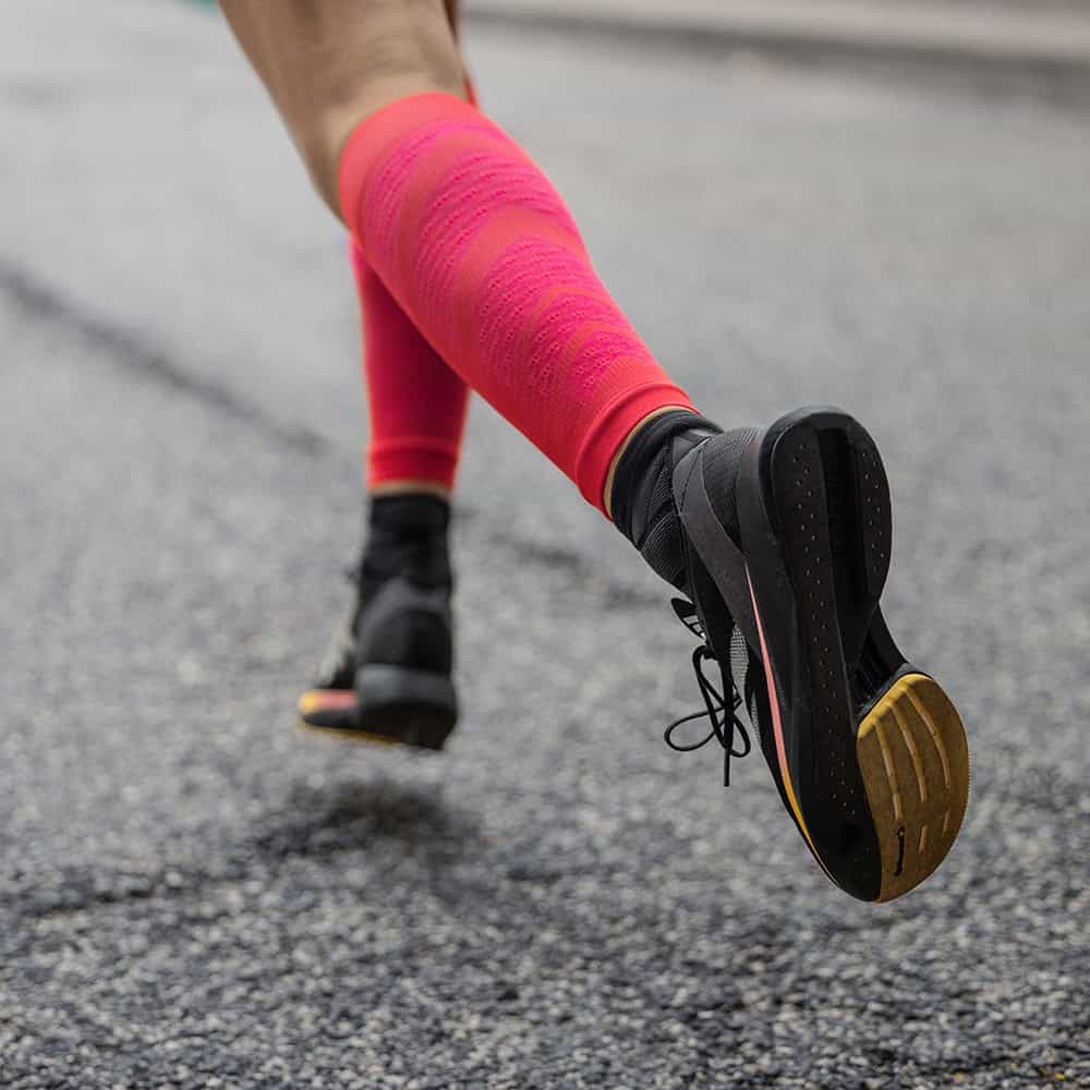 Run Performance Compression Sleeves 5 Hardloopschoenen en felroze compressie kousen tijdens een hardlooptraining op een asfaltweg.