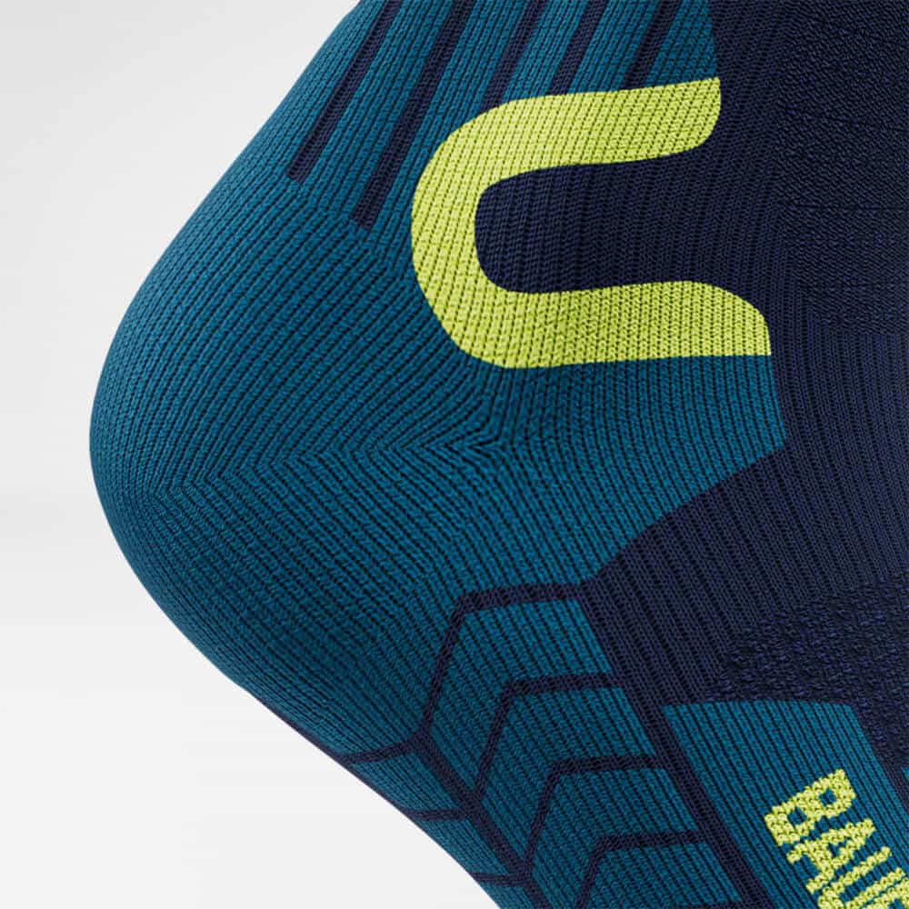 Ski Touring Compression Socks 8 Close to the knee, a pair of sports trousers featuring a pattern in shades of teal and navy with a neon yellow cut-out; plenty of texture is visible; the brand logo and graphic elements are present.