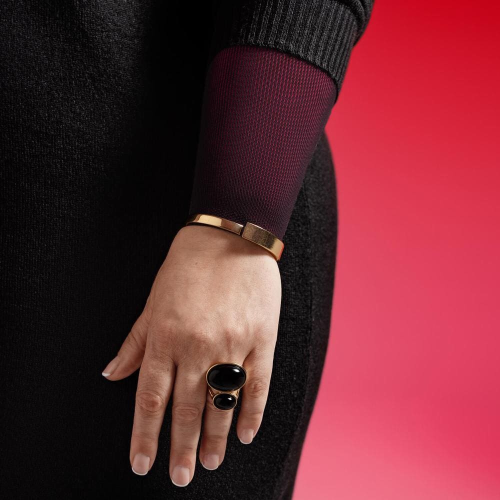 VenoTrain® curaflow armkousen 11 Vrouwelijk hand met stijlvolle sieraden en donker kleding, close-up tegen een roze achtergrond - FrisFysio.nl.